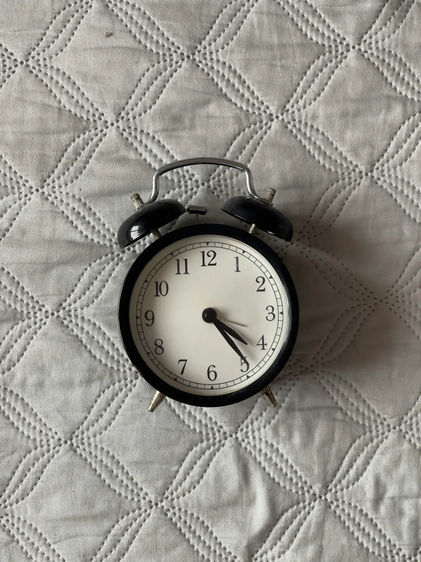 An analog alarm clock resting on bedding