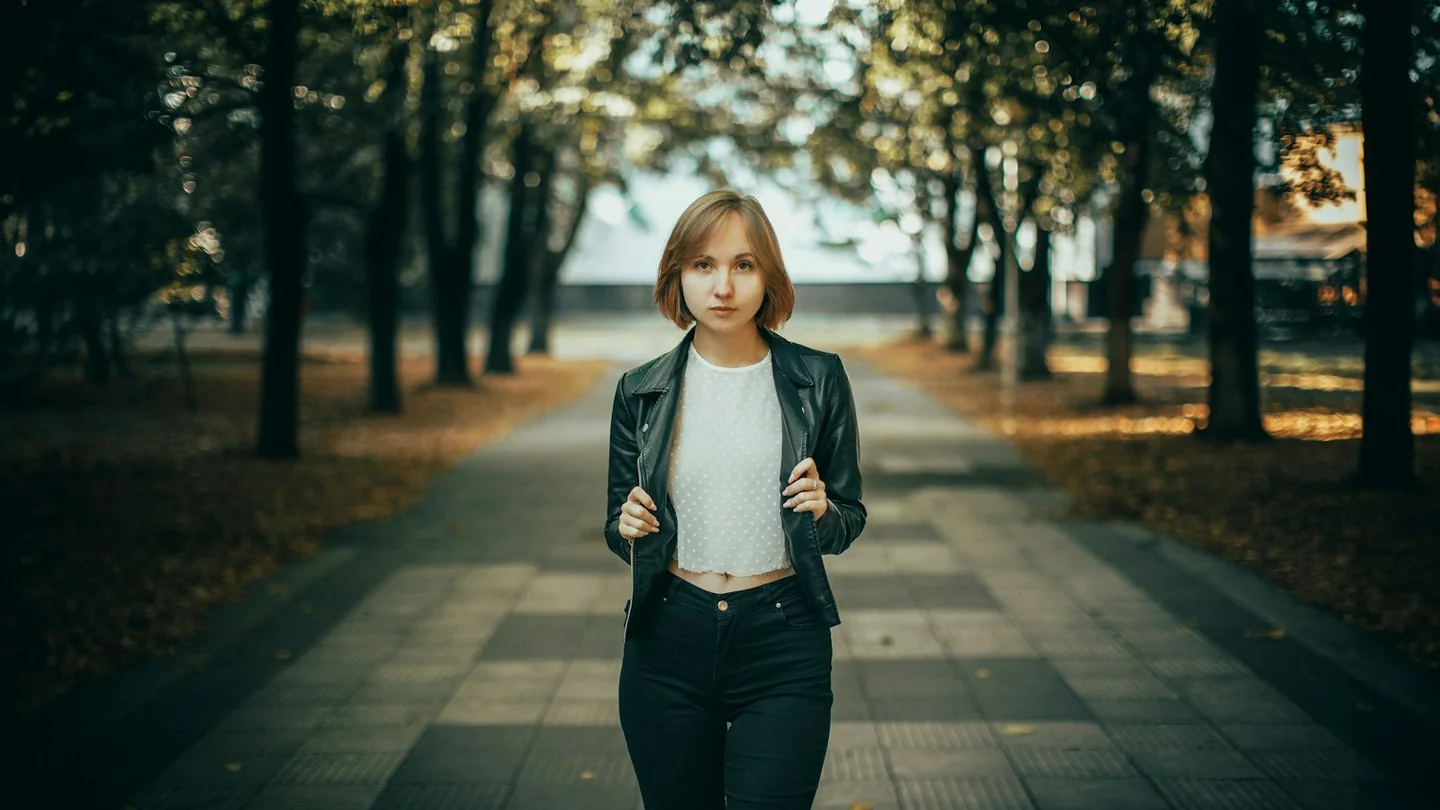 A woman walking along a tree-lined path in autumn