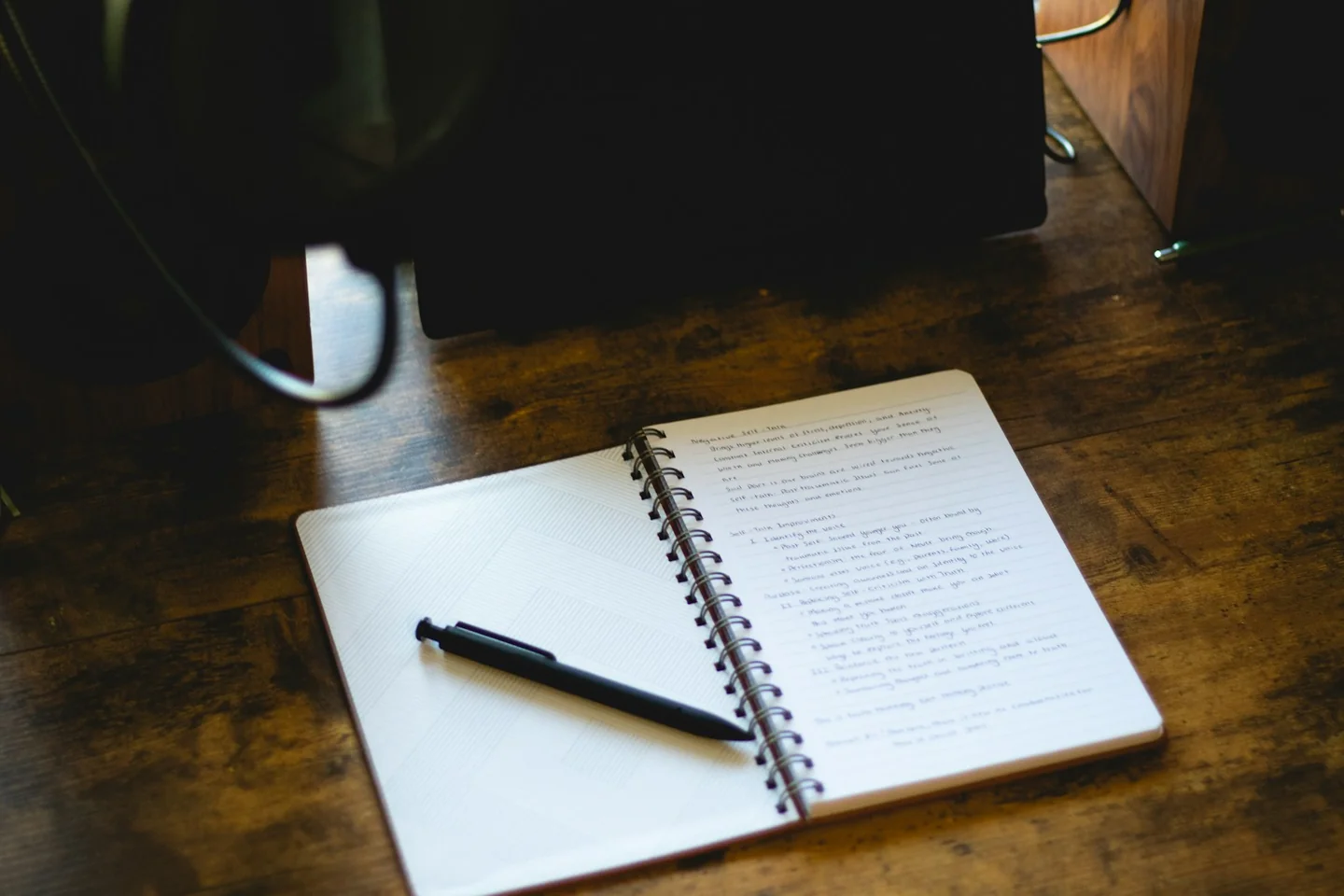 A notebook and pen beside a cup on a wooden desk
