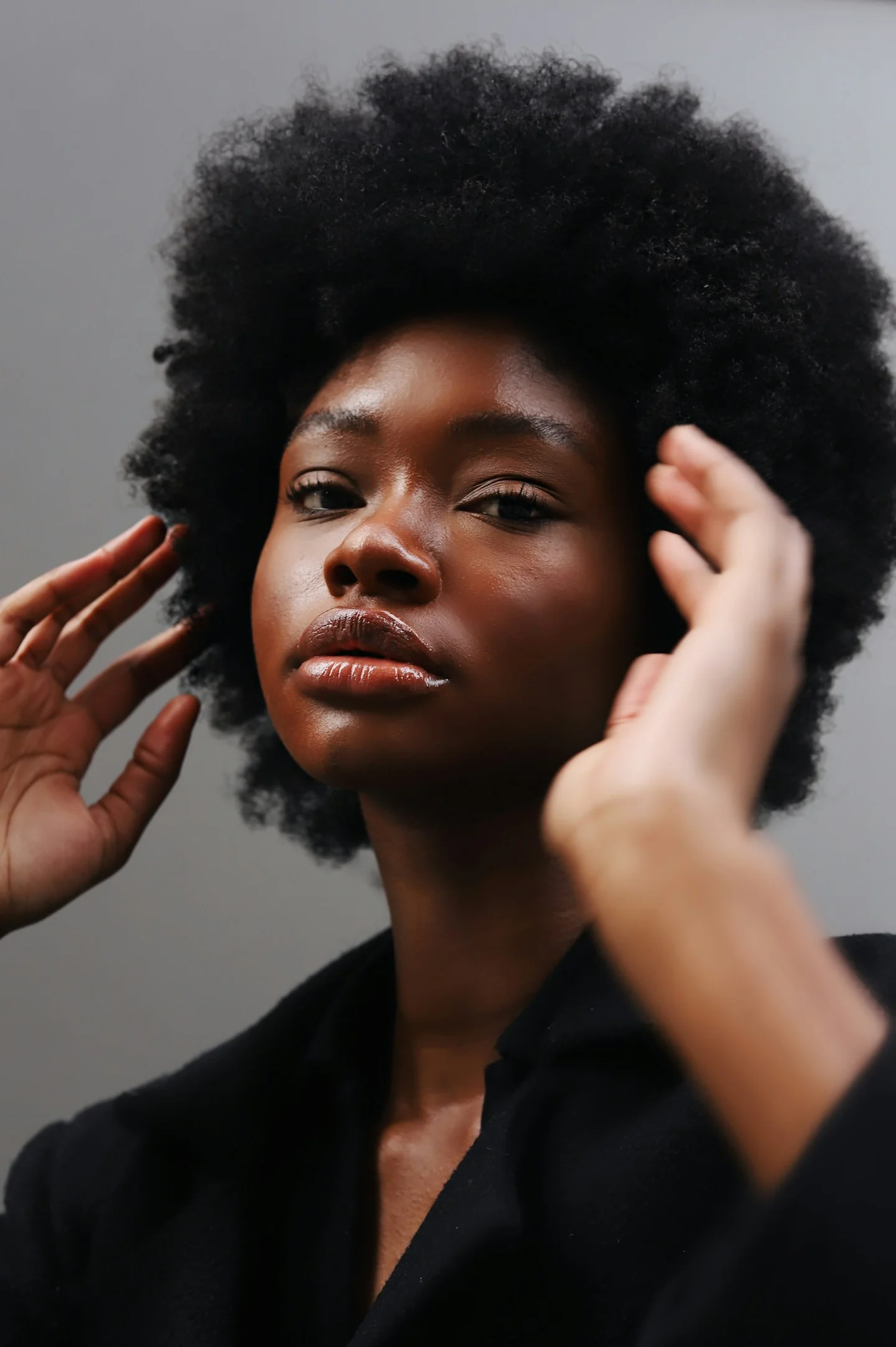 A woman with short textured hair, photographed while adjusting her hair