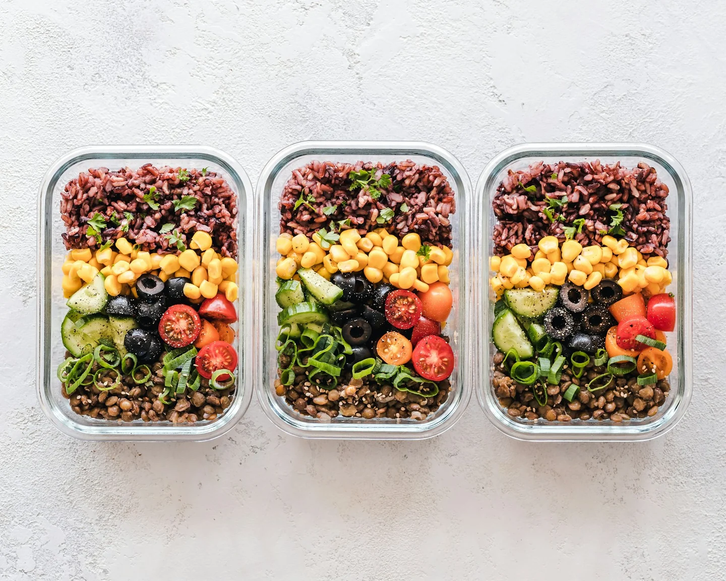 Three containers with grains, vegetables, beans, and other meal components