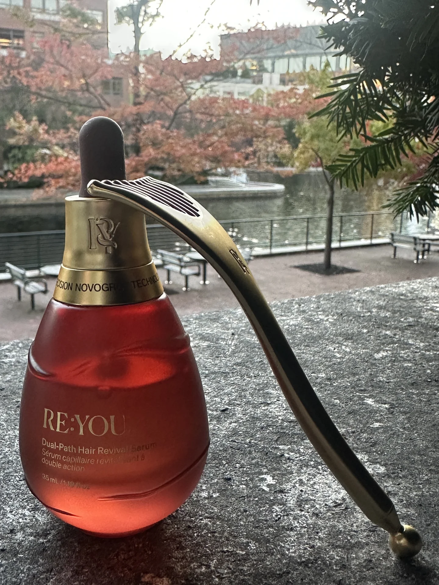 RE:YOU hair serum and gold scalp massager beside autumn foliage