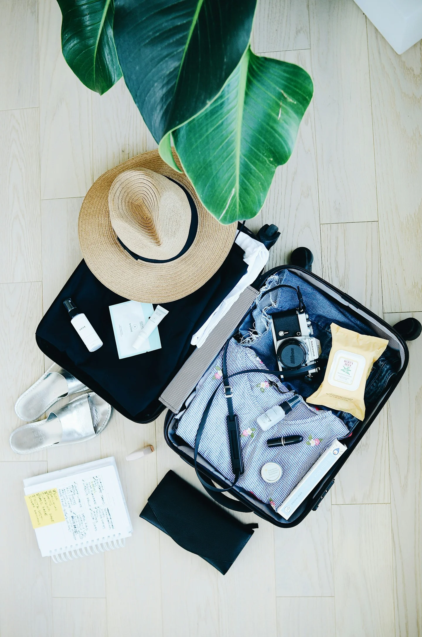 An open suitcase with travel items, folded clothing, and a hat